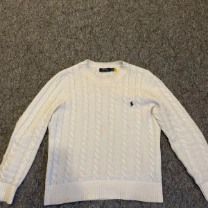 Vit stickad Ralph Lauren tröja - Säljer en klassisk tjock vit cable-knit / kabelstickad Ralph Lauren sweater, i mycket bra skick. Sparsamt använd, säljes i skicket som visas på bild. Skriv gärna vid övriga frågor!