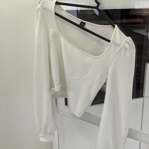 Vit långärmad topp från Shein - Säljer en stilren vit långärmad topp från Shein. Toppen har en unik asymmetrisk design med en bred halsringning och puffiga ärmar. Perfekt för att ge en elegant touch till din outfit.