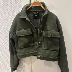 Grön ullblandad jacka från BikBok - Snygg grön jacka från BikBok i ullblandning. Jackan har en croppad design med stora fickor framtill och knappar för stängning.💚