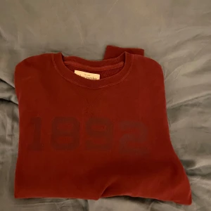 Vinröd tröja från Abercrombie & Fitch - Säljer en snygg vinröd tröja från Abercrombie & Fitch med trycket '1892' på framsidan. Tröjan har en klassisk rund hals och är perfekt för en avslappnad stil.