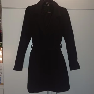 Svart kappa från H&M  - Snygg svart kappa från H&M med knappar och bälte i midjan. Perfekt för kyligare dagar med sin stilrena design och långa ärmar. Passar både XS, S och M.