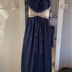 Mörkblå långklänning med paljettdetaljer - Elegant mörkblå långklänning med glittrande paljettdetaljer och spets vid midjan. Klänningen har breda axelband och ett plisserat liv som ger en lyxig känsla..har kostat 3000kr . Storlek är one size motsvarande  smal och en jätte  liten medium 
