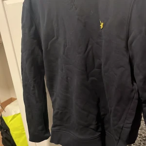 Mörkblå tröja från Lyle & Scott - Säljer en stilren mörkblå tröja från Lyle & Scott med deras ikoniska gula logga på bröstet. Tröjan har långa ärmar och en klassisk rund halsringning. Perfekt för en avslappnad look.