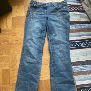 Blå jeans med dekorativa detaljer - Snygga lågmidjade blå jeans med unika dekorationer!! Bootcut stil o väldigt långa i benen  (OBS! Dem har tappat en av kristallerna går att se på bilderna)