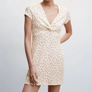 Blommig klänning - Charmig kortklänning i ljus färg med små blommor och knyt framtill. Den har en v-ringad design och korta ärmar, perfekt för sommarens varma dagar. Den är i storlek 36 men skulle säga fungerar som 34 också. Använd 2 gånger