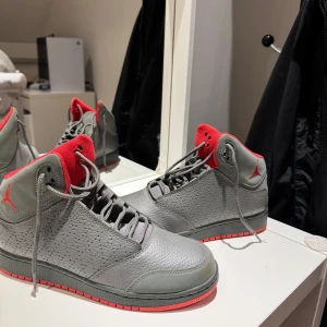 Grå och röda Nike Air Jordans - Säljer ett par grå Nike Air Jordans med röda detaljer. Skorna har en snygg perforerad design och klassisk snörning. Perfekta för både vardag och fest! De är i mycket bra skick och redo för nya äventyr.