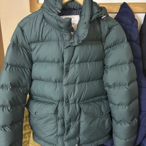 Grön dunjacka från Woolrich - Säljer en snygg grön dunjacka från Woolrich i storlek S. 10/10 skick. Nypris är ca 6000 kr. Perfekt för kalla vinterdagar med sin varma och quiltade design. Den har både dragkedja och knappar för extra skydd mot kylan. Passar perfekt för både vardag och utomhusaktiviteter. Priset är möjligt att diskuteras😊