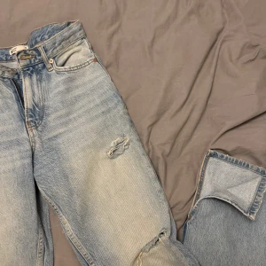 Blå jeans med slitningar - Säljer ett par klassiska blå jeans från Gina  i bra skick. De har coola slitningar på knäna och en avslappnad passform. Perfekta för en casual look!  Slits i benen, storlek 36