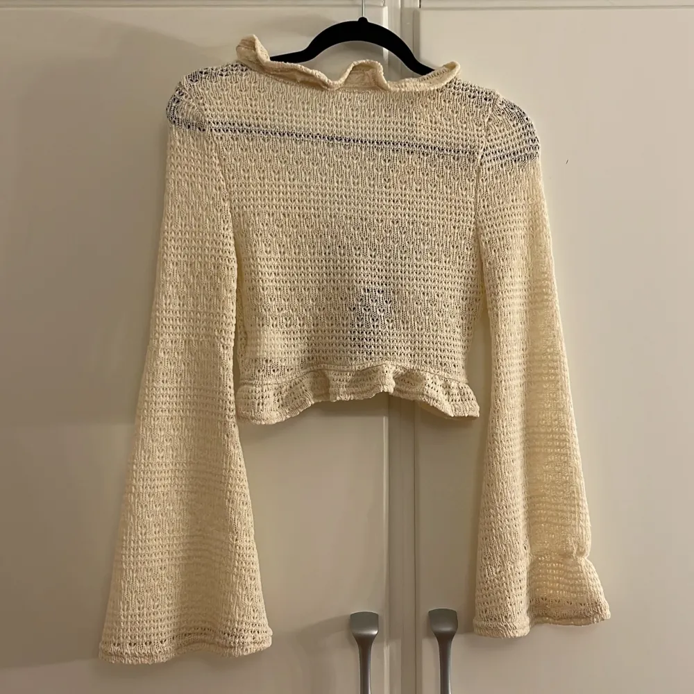 Säljer en superfin beige stickad kofta med volangdetaljer och en stor svart rosett framtill. Den är croppad och har långa ärmar som ger en elegant look. Perfekt för höst och vår när du vill ha något lätt men ändå stiligt. Passar både till vardags och fest!. Tröjor & Koftor.