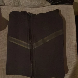 Svart hoodie från Nike - Säljer en svart hoodie från Nike i mycket bra skick. Den har en dragkedja framtill och en huva. Perfekt för höst och vår, med en stilren design och diskreta detaljer. Passar både till träning och vardagsbruk.