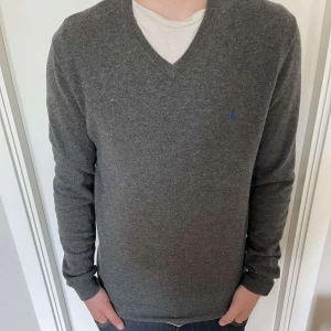 Grå tröja från Polo Ralph Lauren - Säljer en stilren grå tröja från Polo Ralph Lauren i storlek M. Tröjan har en klassisk v-ringning och är perfekt för både vardag och lite finare tillfällen. Den är i mycket bra skick och har en liten broderad logga på bröstet. Passar perfekt till höst och vinter! Nypris ca 2000kr, Vårat pris 259kr!