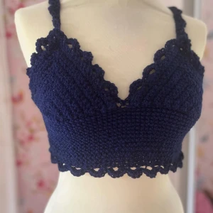 Mörkblå virkad topp - Säljer en superfin mörkblå virkad topp med spetsdetaljer. Den är perfekt för sommardagar och har en söt, croppad stil. Toppen är ärmlös och har en v-ringad design som ger en bohemisk känsla. Passar perfekt till festivaler eller en dag på stranden!
