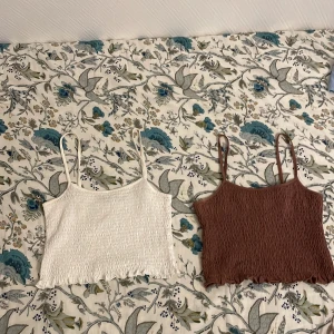 Två smockade linnen från Bik Bok - Säljer två supersöta smockade linnen från Bik Bok i storlek S. Ett är vitt och det andra är brunt. Båda har smala axelband och en vågig kant nertill. Perfekta för sommardagar eller att styla med en kofta för hösten. 🧡20kr st