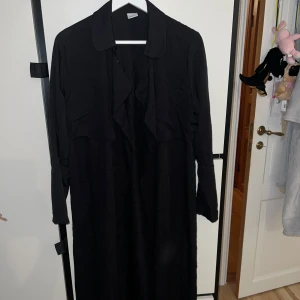 Svart kappa från Gina Tricot - Säljer en stilren svart kappa från Gina Tricot i storlek 38. Perfekt för höst och vår, med långa ärmar och en klassisk krage. Den har en elegant och tidlös design som passar till alla tillfällen. Ett måste i garderoben för den modeintresserade!