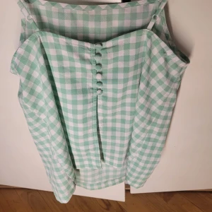 Grön- och vitrutigt linne från ASOS - Säljer ett superfint grönt och vitt rutigt linne från ASOS. Det har justerbara axelband och knappar framtill som en söt detalj. Perfekt för sommardagar eller en avslappnad vårlook. Materialet känns lätt och luftigt, perfekt för varmare väder!