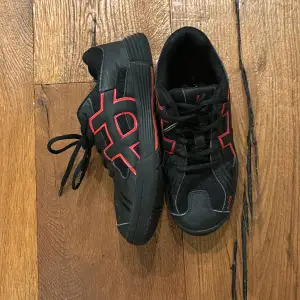 Säljer ett par coola svarta sneakers från Unihoc med röda detaljer. Skorna har snörning och är i syntetmaterial, perfekt för inomhussporter. De är i bra skick och redo för nya äventyr. Passar perfekt för träning eller vardagsbruk!