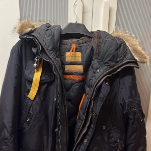 Svart vinterjacka från Parajumpers - Säljer en svart Parajumpers vinterjacka i storlek L. Jackan har en avtagbar huva med pälsdetaljer och flera praktiska fickor. Den är i bra skick men har ett litet slitage på ena ärmen. Perfekt för kalla vinterdagar! ❄️Köpte den för 10 000 kronor ett år tillbaka därför säljer jag den för 2500