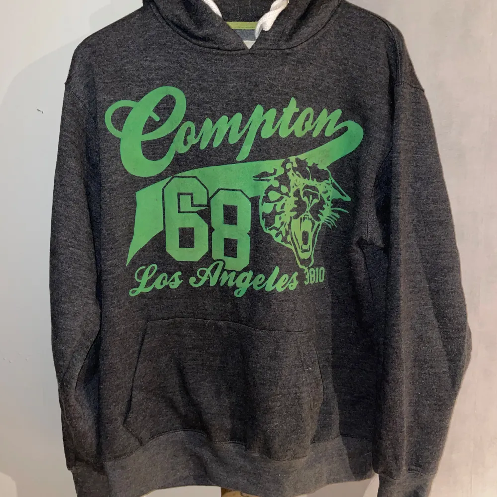 Säljer en grå hoodie från Denim Day i storlek large. Den har en cool grön text och grafik med 'Compton 168 Los Angeles' på framsidan. Perfekt för en avslappnad stil med känguruficka och justerbar huva. Passar bra till både höst och vår.. Hoodies.