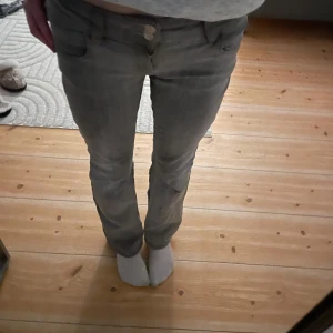 Gråa bootcut jeans - Säljer ett par grå jeansbyxor i bra skick. De har en tight passform och är lågmidjade med knappar fram. Perfekta för vardagsbruk och kan matchas med det mesta i garderoben. De har även ett litet litet hål på knät men inget man tänker på.