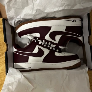 Nike Air Force 1 i vinrött och vitt - Säljer ett par snygga Nike Air Force i vinrött och vitt. Skorna är i nytt skick