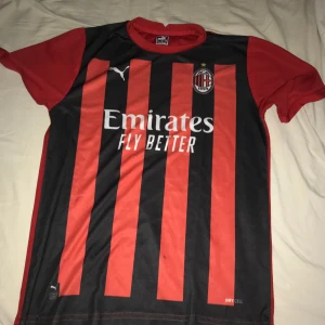 AC Milan fotbollströja från Puma - Säljer en AC Milan fotbollströja i svart och rött från Puma. Tröjan har korta ärmar och är i randigt mönster med klubbens emblem på bröstet. Den är i bra skick och perfekt för alla Milan-fans! 🖤❤️