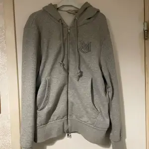 Säljer en snygg grå hoodie från Moncler i mycket bra skick. Den har en dragkedja framtill och en broderad logga på bröstet. Perfekt för höst och vår, med en skön passform och praktiska fickor. Huvan har justerbara snören för extra komfort. Perfekt för en casual look!