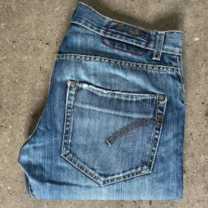 Ljusblå dondup jeans  - Säljer ett par snygga blå jeans i bra skick. De har en slim passform  och är perfekta för både vardag och fest. Jeansen har en cool broderad detalj på bakfickan och är tillverkade i slitstarkt denim. Perfekta för höst och vår! Med slitningar som är en del av design!