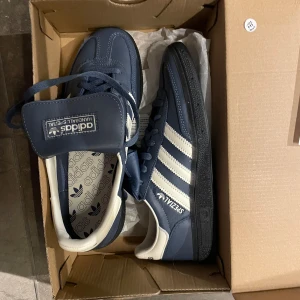 Adidas Spezial sneakers - Säljer ett par Adidas Spezial sneakers i blått och vitt. Skorna är helt nya och kommer i originalkartong med prislapp kvar!  De har en klassisk design med tre vita ränder på sidan och en robust svart sula. Perfekta för både vardag och sportiga tillfällen!