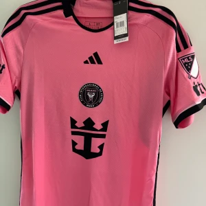 Fotbollströja från Inter Miami Messi  - Säljer en snygg rosa fotbollströja från Inter Miami med Messi och nummer 10 på ryggen. Tröjan har korta ärmar och svarta detaljer, inklusive klubbens emblem och MLS-logga. Storlek large