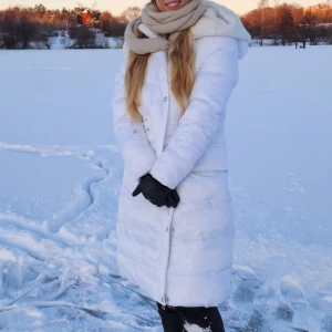 Vit lång puffjacka/kappa med huva - Säljer en supermysig vit lång jacka med huva, perfekt för kalla vinterdagar nu. Jackan har långa ärmar och stängs med dragkedja och knappar. Den är i mycket bra skick och håller dig varm och stilren hela vintern. Passar perfekt för både vardag och vinterpromenader! ❄️ storlek S men passar på alla mellan Xs-M skulle jag säga.