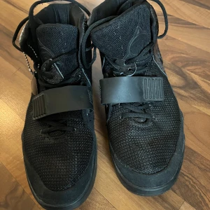 Svarta sneakers med snörning och rem - Säljer ett par svarta sneakers i bra skick. De har en cool design med snörning och en bred rem över foten. Skorna är gjorda av syntetmaterial och har en texturerad yta. Perfekta för både vardag och fest! Köpta på någon marknad så inga orginal nike skor.