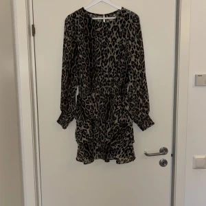 Leopardmönstrad klänning - Snygg leopardmönstrad klänning med långa ärmar och volangdetaljer. Perfekt för en utekväll eller fest! Den har en elastisk midja för en bekväm passform och är gjord i ett lätt material.