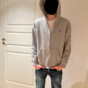  Ralph loren grå hoodie - Säljer en stilren grå hoodie från Polo Ralph Lauren. Den har en dragkedja framtill och en liten broderad logga på bröstet. Perfekt för en avslappnad stil och passar till de flesta tillfällen. Superbekväm och i bra skick!