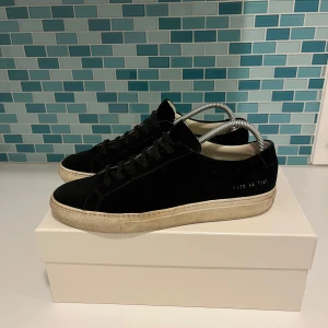 Svarta sneakers från Common Projects - Säljer ett par stilrena svarta sneakers från Common Projects i modellen Achilles Low. Skorna är i mocka och har en klassisk design med snörning. De är i använt skick, hör av dig vid frågor. (Priset kan diskuteras)