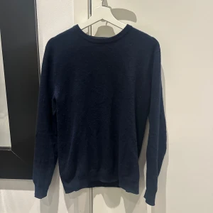 Mörkblå kashmirtröja från John Henric - Säljer en supermjuk och stilren mörkblå kashmirtröja från John Henric. Perfekt för både vardag och festliga tillfällen. Tröjan har en klassisk passform med långa ärmar och rund hals. Ett måste i garderoben för den som älskar kvalitet och komfort.