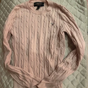 Rosa stickad tröja från GANT - Säljer en superfin rosa stickad tröja från GANT i storlek XS. Den har ett klassiskt kabelstickat mönster och är perfekt för både höst och vår. Tröjan är i mycket bra skick och gjord av stretchig bomull för extra komfort. Perfekt för en stilren och mysig look! 💖