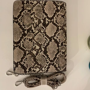 Ormmönstrad kuvertväska - Säljer en supercool kuvertväska med ormmönster. Den har en avtagbar kedjerem och stängs med en knapp. Perfekt för en utekväll eller fest! 🐍✨