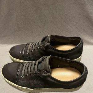 Gråa sneakers från Lanvin - Säljer ett par svarta sneakers från Lanvin i bra skick. Skorna har en stilren design med snörning och en vit sula som ger en snygg kontrast. Perfekta för både vardag och fest. Passar till det mesta i garderoben!