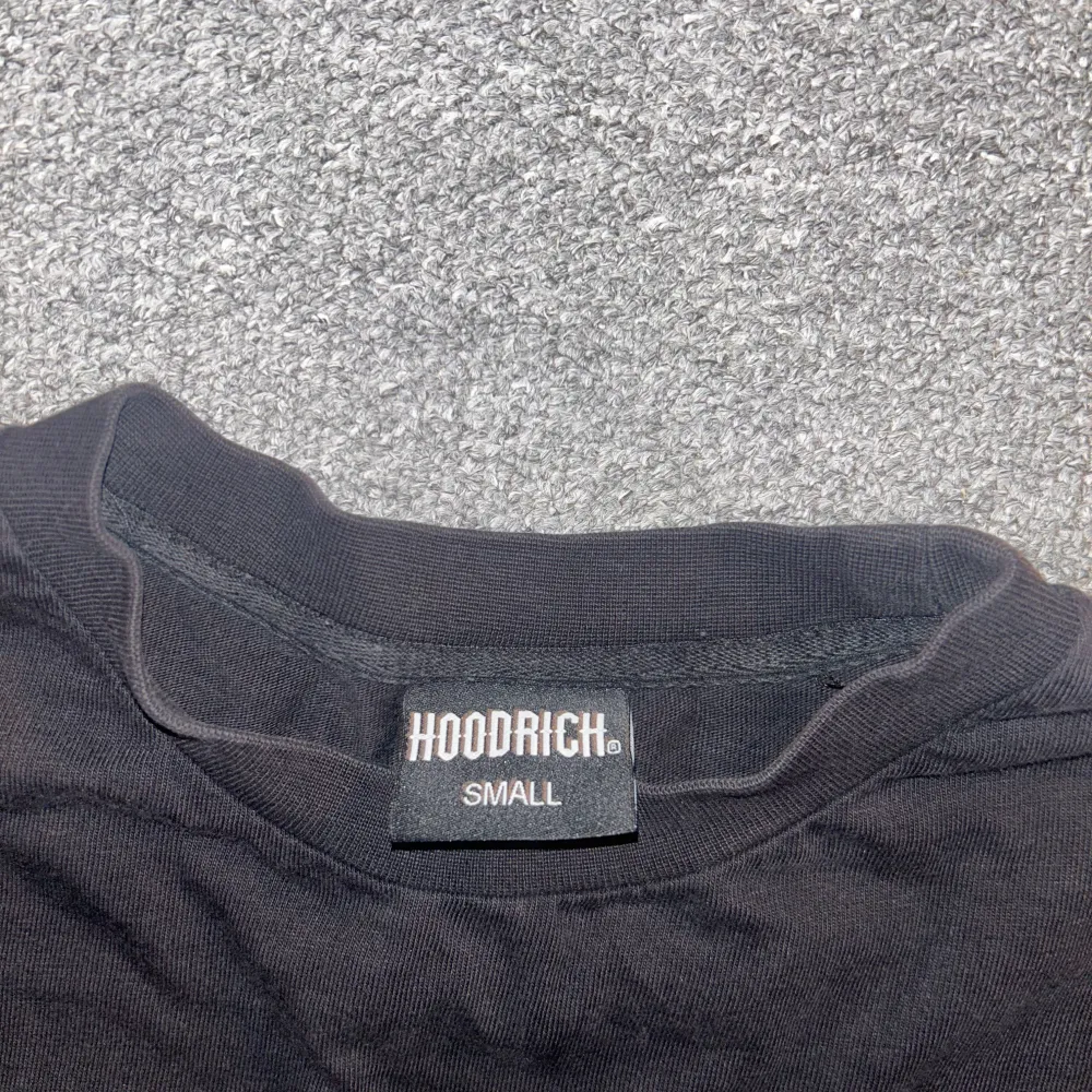 Säljer en svart t-shirt från Hoodrich i storlek S. Den har tryck både fram och bak med texten 'HOODRICH' och detaljer i rött och grått. Perfekt för en casual look eller streetwear-stil. T-shirten är i bra skick och redo för nya äventyr.. T-shirts.