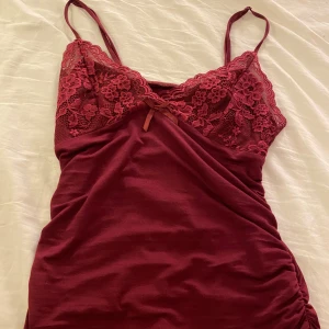 Supergulligt spetslinne  - Säljer ett supervackert vinrött linne med spetsdetaljer. Det har smala axelband och en söt liten rosett framtill. Säljer endast vid bra bud. 