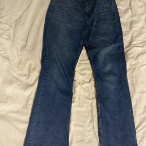 Blå lågmidja  bootcut jeans - Säljer ett par klassiska blå bootcut jeans i storlek M. De har en snygg och tidlös design med normal passform och är perfekta för både vardag och fest. Jeansen är i bra skick och har en knapp och dragkedja framtill.