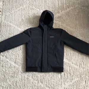 Carhartt Hooded Sail Jacket - Säljer en svart windbreaker från Carhartt i storlek S. Jackan är i princip oanvänd och skicket är som ny. Nypris 2600