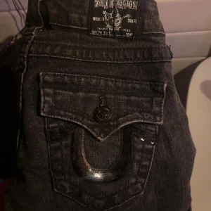 Grå lowrise flare True Religion - Säljer ett par snygga grå jeans från True Religion i flare modell och låg midja, strl 24. De har coola detaljer med knappar och en unik design på bakfickorna. Perfekt skick!!🥰🙏🏻