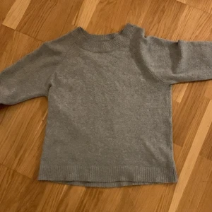 Grå stickad tröja från Vero Moda - Mysig grå stickad tröja från Vero Moda i storlek M. Tröjan har långa ärmar och ribbade muddar vid ärmslut och nederkant. Den är lite nopprig 