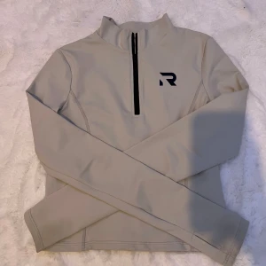 Beige långärmad tröja från Relode - Säljer en beige långärmad tröja från märket R. Tröjan är tillverkad i 90% nylon och 10% spandex, vilket gör den stretchig och bekväm. Den har en dragkedja framtill och är perfekt för kyligare dagar. Passar bra till både vardag och träning.