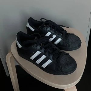 Svarta och vita Adidas Superstar - Säljer ett par klassiska Adidas Superstar i svart. De är i bra skick och i storlek 38 2/3. 