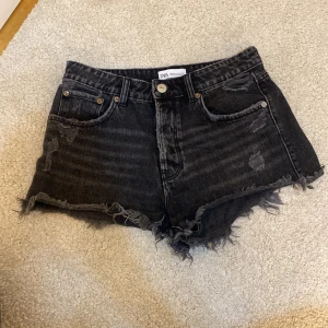 Svarta jeansshorts från Zara - Säljer ett par coola svarta jeansshorts från Zara i storlek 36. De har en snygg slitning och fransiga kanter för en avslappnad look. Perfekta för sommaren och festivaler! 🖤