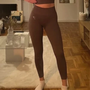 Bruna leggings från Gymshark - Säljer ett par bruna leggings från Gymshark i mycket bra skick. De är högmidjade och har en tight passform, perfekta för träning eller en avslappnad dag hemma. Materialet är stretchigt och bekvämt, vilket gör dem till ett måste i garderoben. Passar perfekt för höst och vinter!