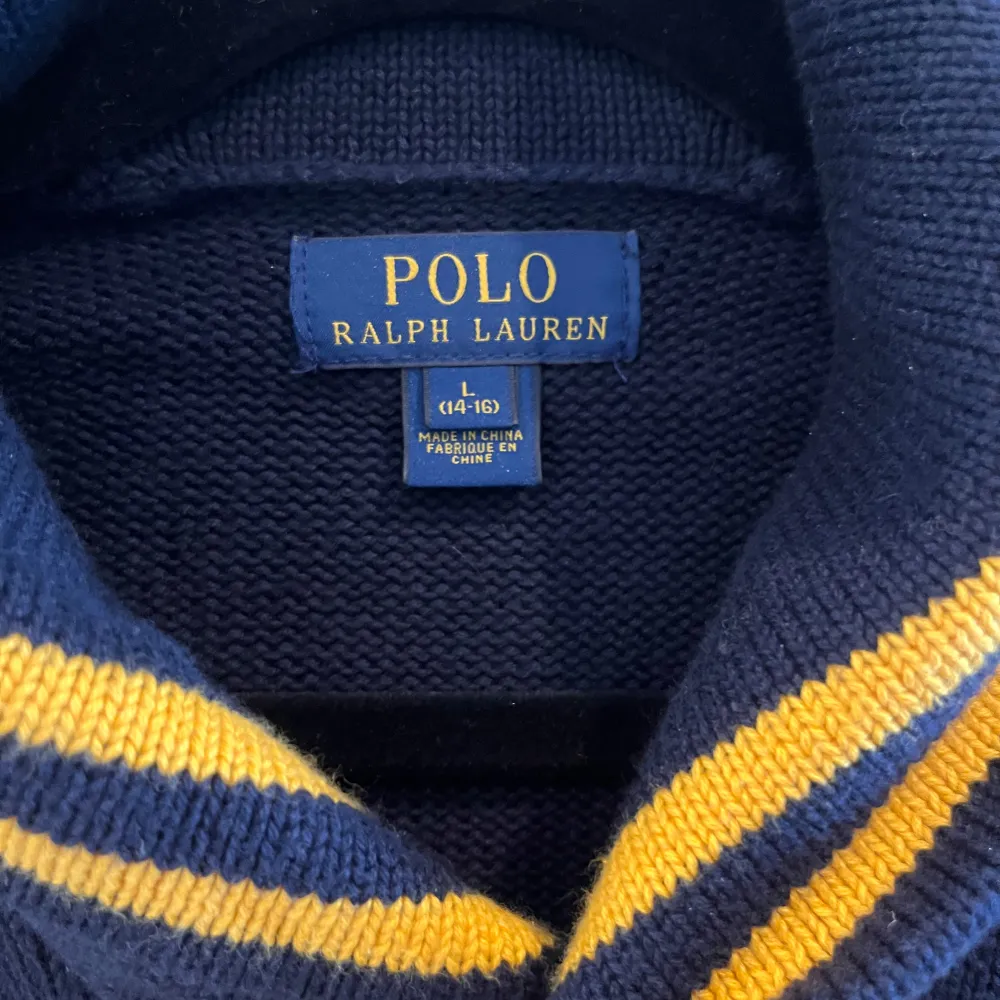 Säljer en snygg mörkblå tröja från Polo Ralph Lauren med en bred gul rand över bröstet och det klassiska logotypen. Tröjan har långa ärmar och en skön krage. Perfekt för höst och vinter!. Tröjor & Koftor.