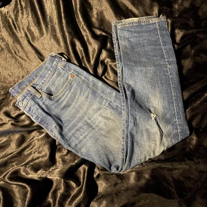 Blå jeans från Levi's - Säljer ett par klassiska blå Levi's jeans i modell 501. De är i bra skick med en liten slitage på ena benet för en cool look. Perfekta för både vardag och fest! Passar till allt och är superbekväma. 🕺slitaget är original och inte riktiga.
